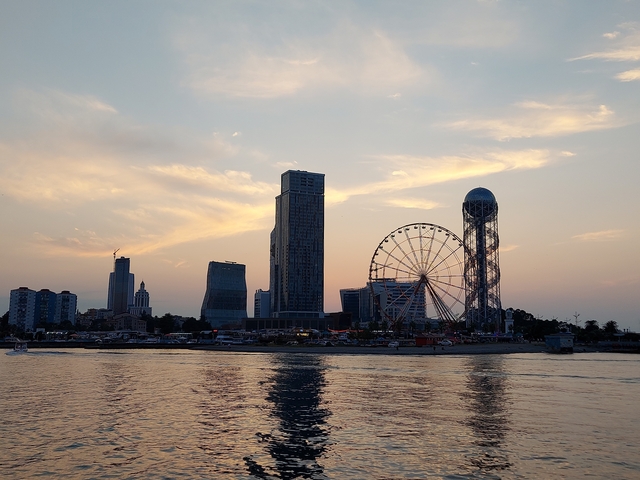 City skyline at sunset with a ferris wheel and tall buildings.
