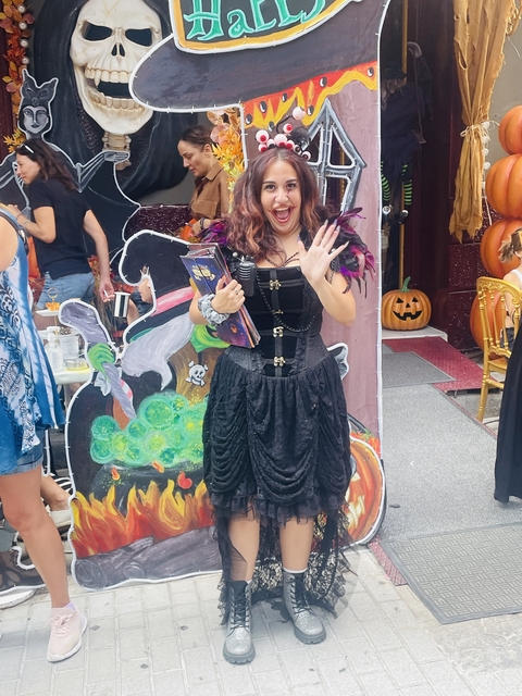 Person in costume waving at the camera with pumpkins around.