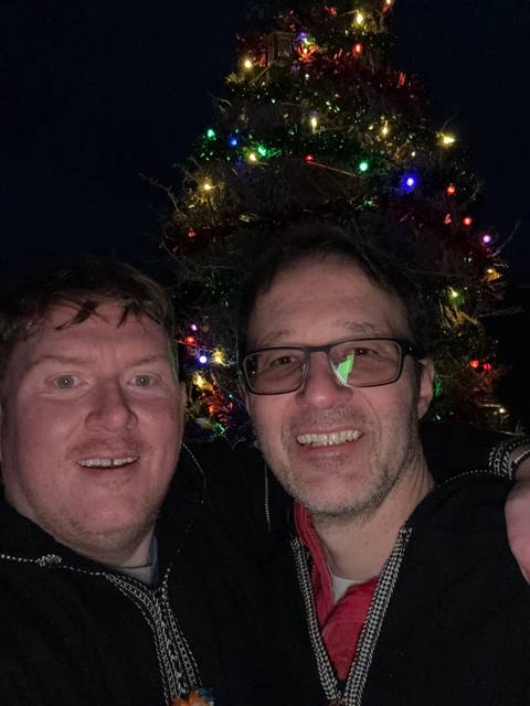Two people smiling in front of colorful holiday lights.