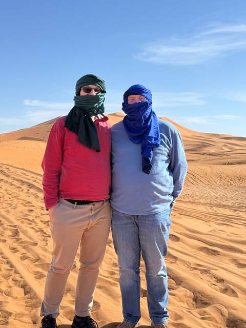 Two people wearing scarves on a sandy desert.