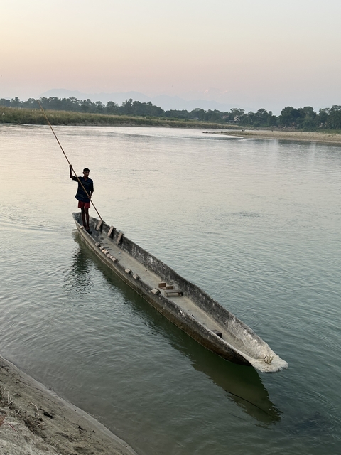 Person standing on a small wooden boat in a river.