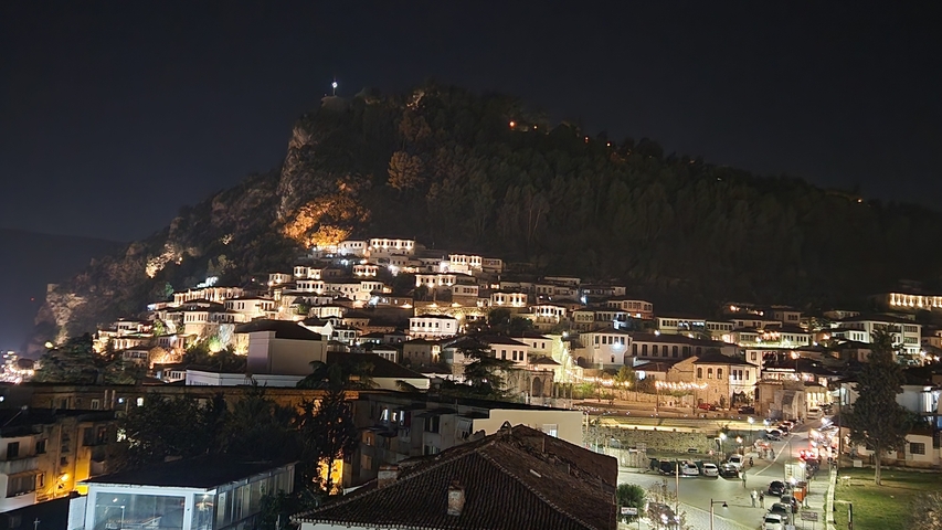 Night view of a town built on a hillside with bright lights.