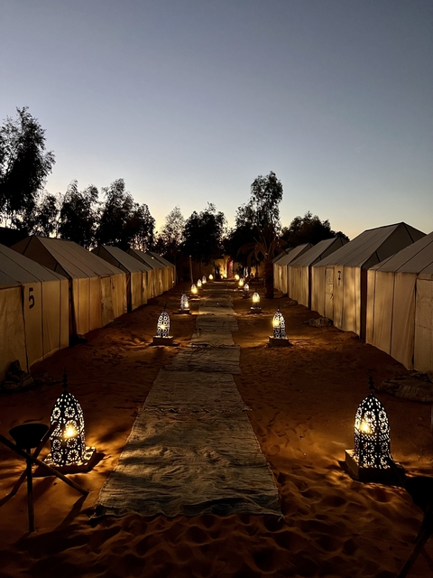 A desert glamping site with lit lanterns and tents in rows at dusk.