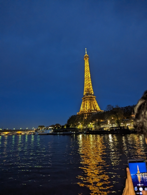 Eiffel Tower lit up at night, seen from the Seine River.