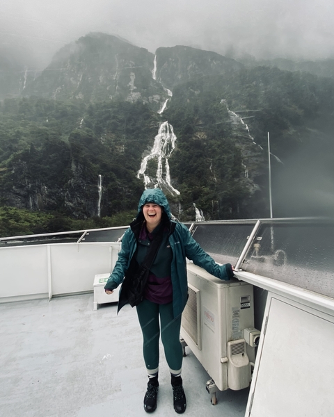 Person in a raincoat smiling on a boat with waterfalls in the background.