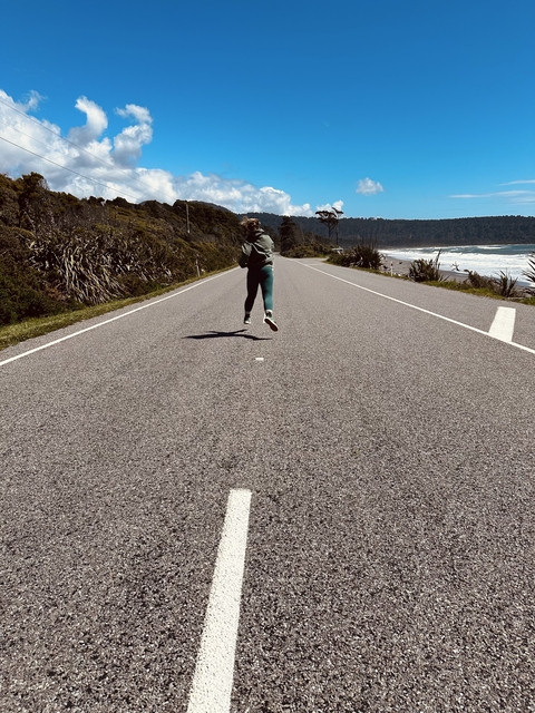 Person jumping on a road by the sea under blue skies.