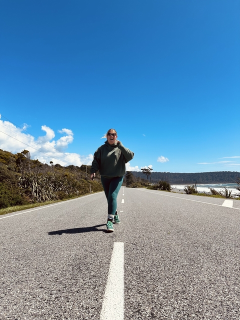 Person walking on a road by the coastline on a sunny day.