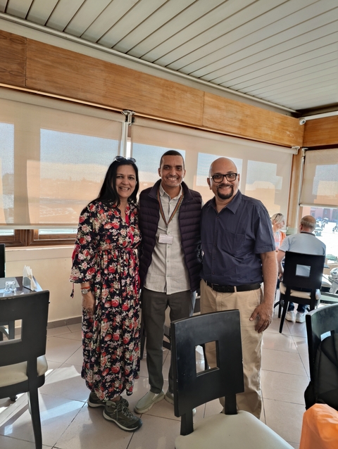 Three people standing together indoors with a cafe setting.