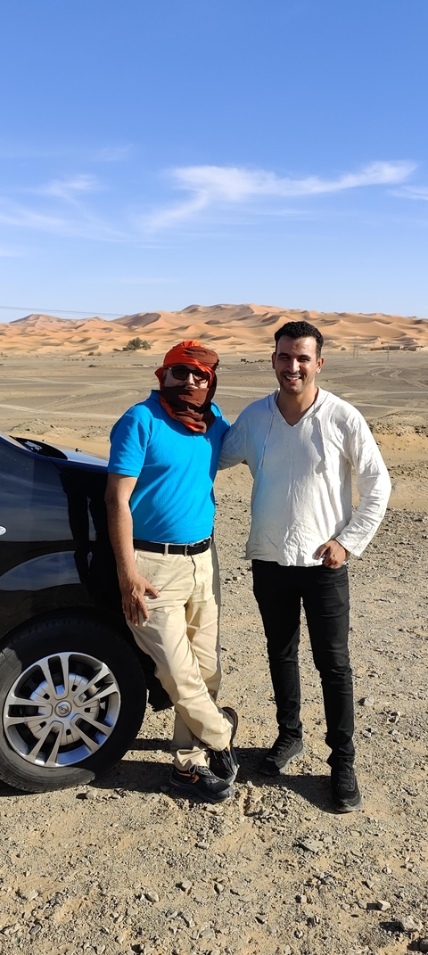 Two people standing next to a car in a desert setting.