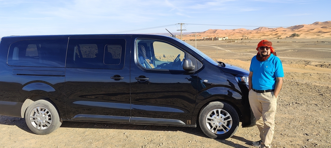 Man standing beside a van with a desert background.