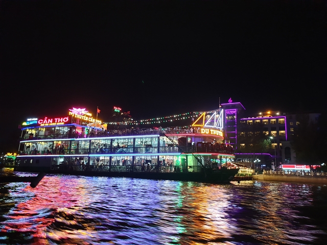 A colorful, lit-up riverboat at night with city lights reflecting on the water.