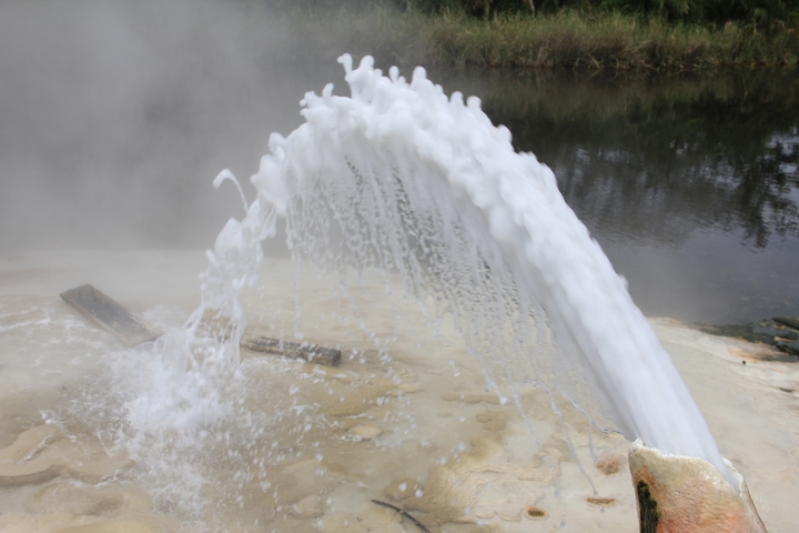 Geyser erupting with steam in the background.