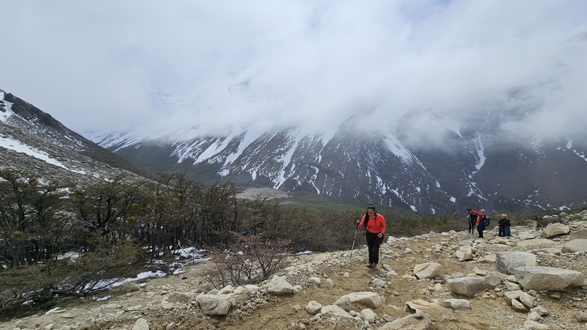 Hikers climbing a rocky trail with a snowy mountain in the background.
