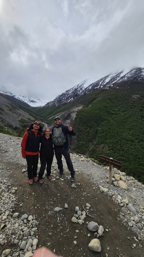 Three people smiling with snow-capped mountains in the background.