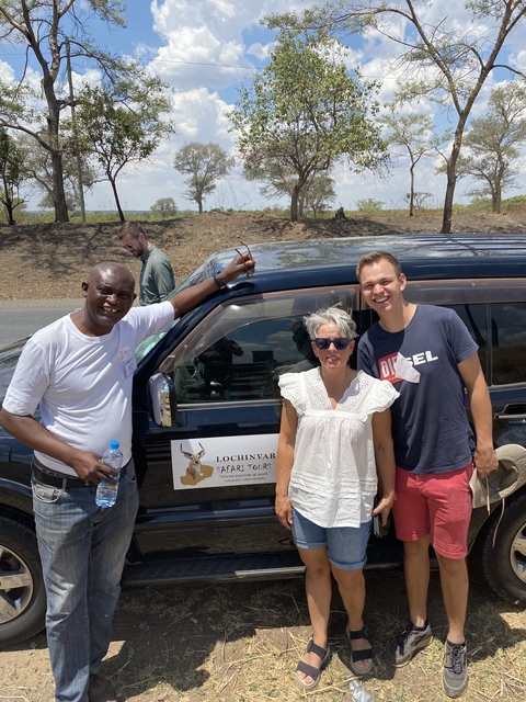 Three people standing beside a safari vehicle.