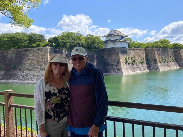 Two people posing in front of a traditional castle and moat.