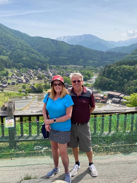Two people overlooking a traditional Japanese village from a high vantage point.