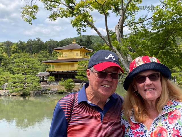 Couple posing in front of Kinkaku-ji, a gold pavilion in a garden.