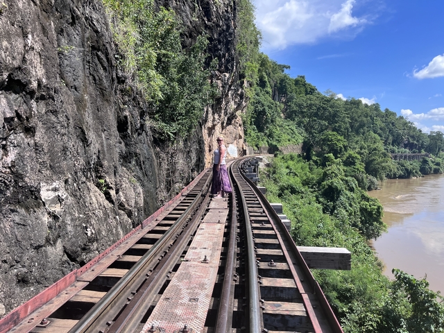 Two people walking on a historic railway track along a river and cliffs.