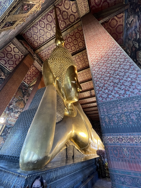 Golden Buddha statue indoors with intricate patterns on the wall.