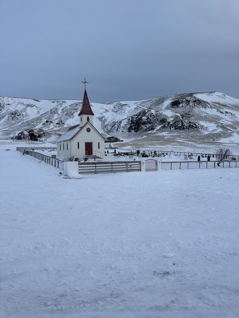 A small church and graveyard covered in snow, surrounded by hills.