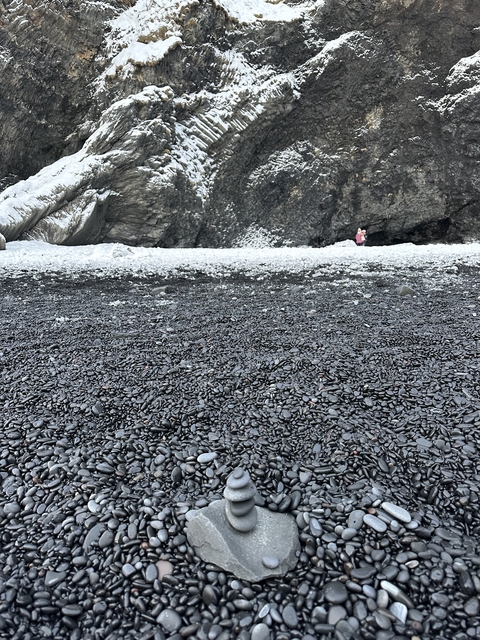 A black pebble beach with rocky cliffs.