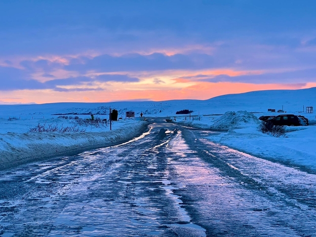 A snowy road leading into a colorful horizon at sunset.
