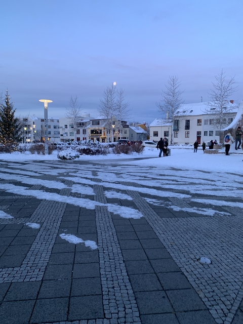 A snowy urban area with people walking near decorated trees.