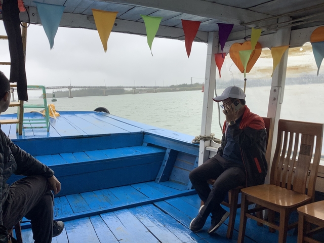 People sitting on a boat on a river with a bridge in the background.