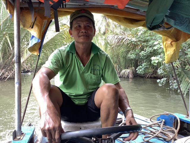 Man sitting in a boat on a waterway lined with trees.