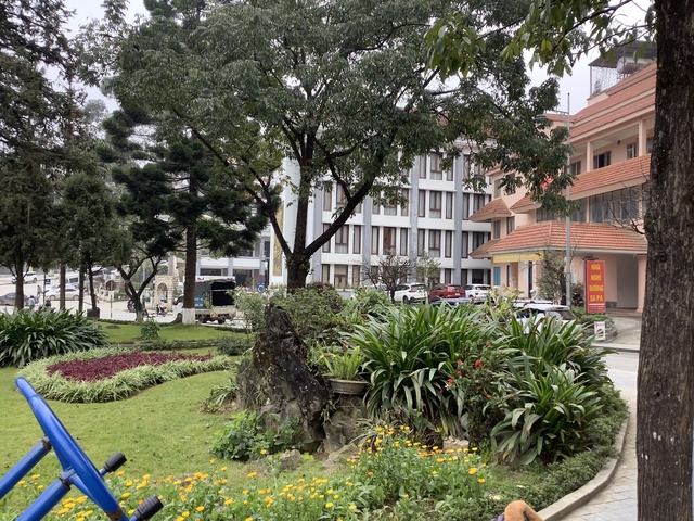 Urban park with gardens and trees, people strolling.