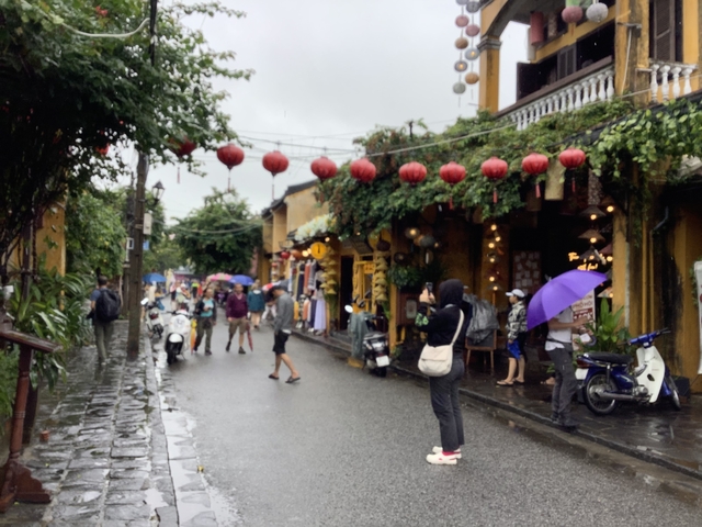 Rainy street with lantern decorations and pedestrians.
