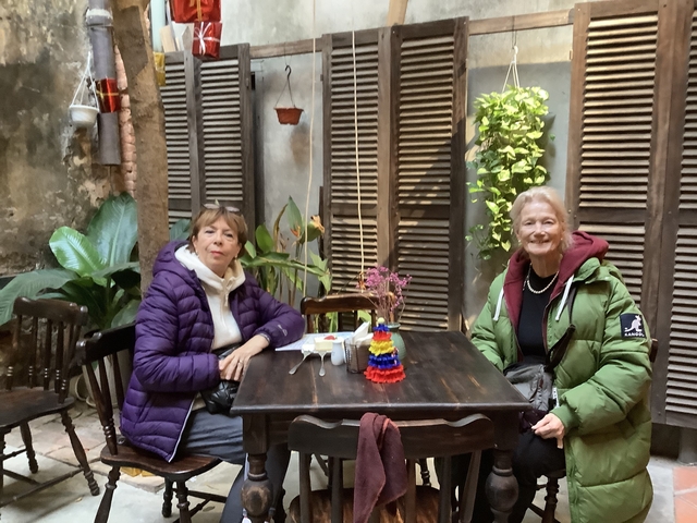Two women sitting at a table in a cafe with plants.