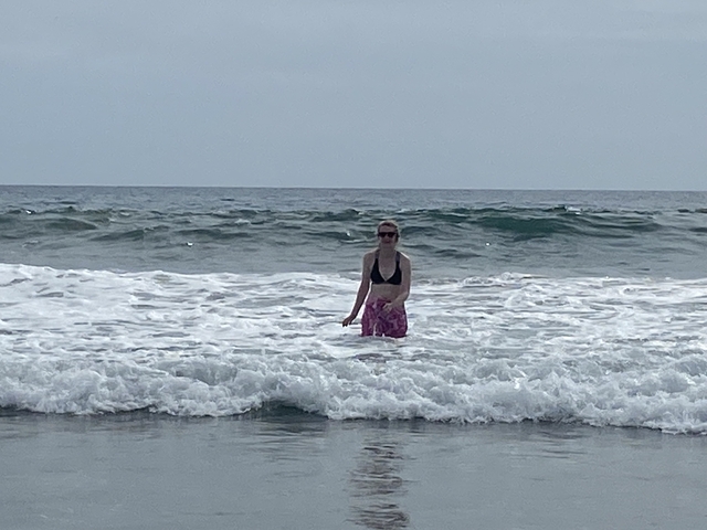 Individual standing waist-deep in ocean waves wearing sunglasses.