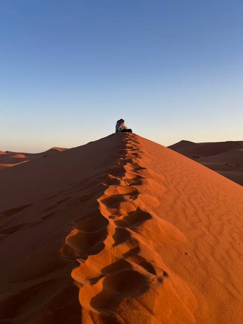 Footprints on a sand dune under a clear sky.