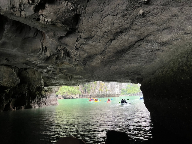 Kayakers paddling through a cave opening into serene waters.