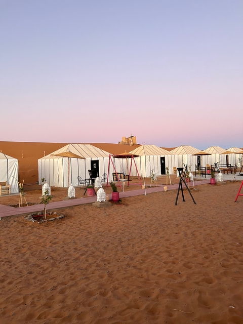 Desert camp with white tents and a pink sky background.