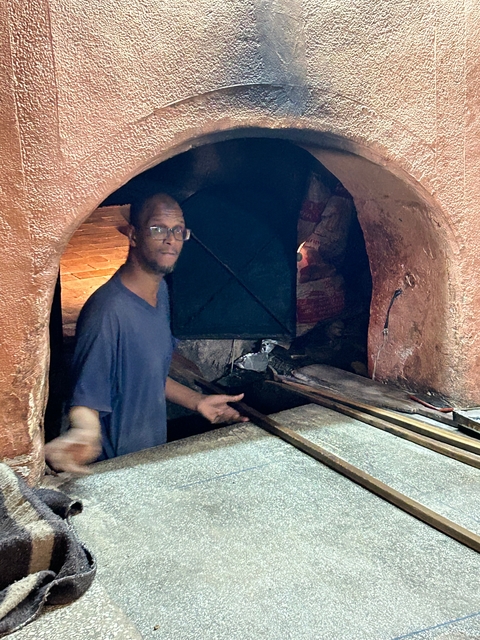 Person preparing a wood-fired oven in a rustic setting.