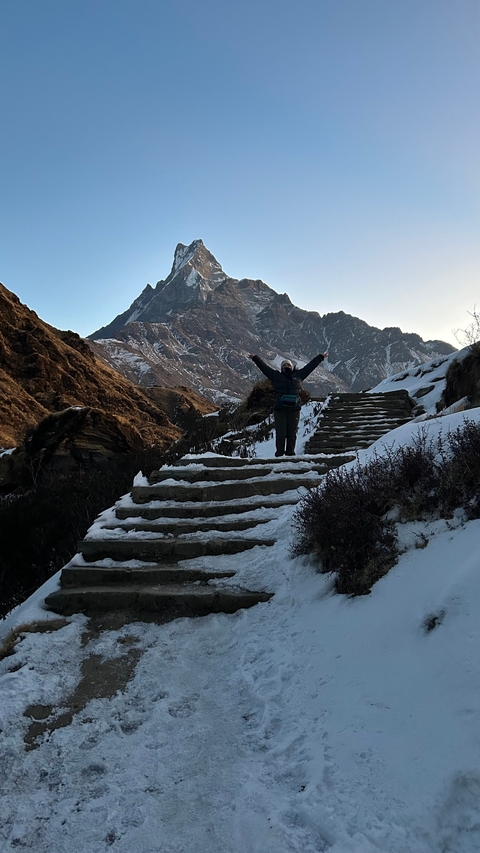 Person standing with arms raised on snow-covered steps.