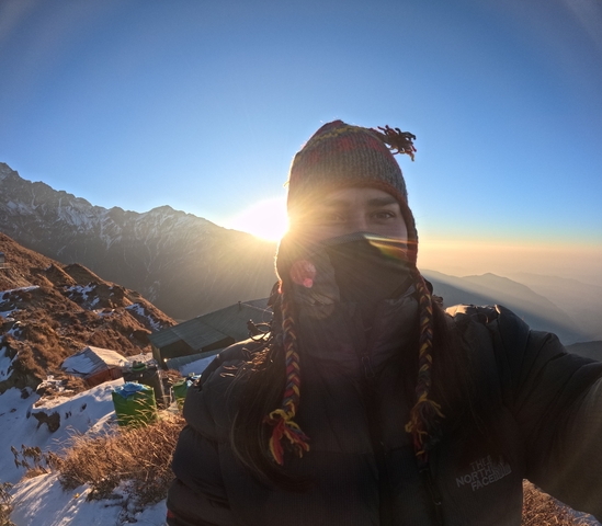 Person taking a selfie with sun and mountains in the background.