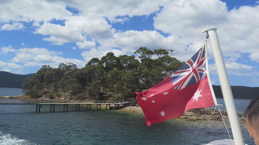 Boat with an Australian flag sailing past a dock.