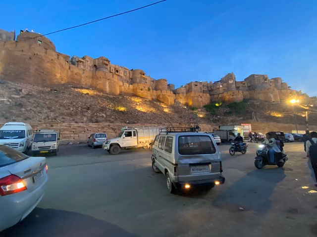 View of a fort lit at twilight with vehicles parked in the foreground.