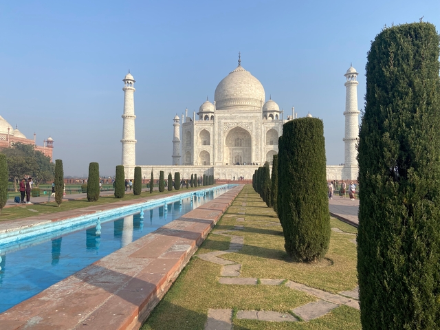 The Taj Mahal surrounded by gardens and visitors during the day.