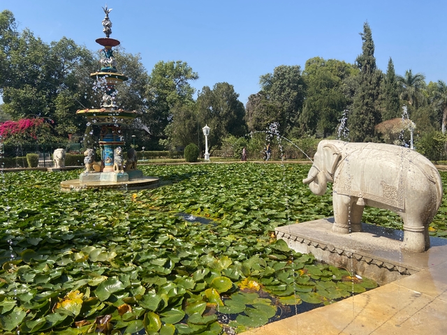 Beautiful garden with fountains and elephant statues surrounded by trees.