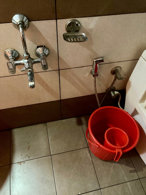 A bathroom with red bucket and faucet.