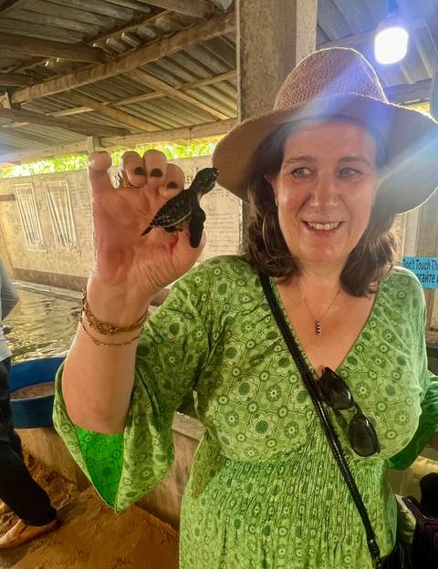 A woman holding a small turtle, standing in front of a mural.