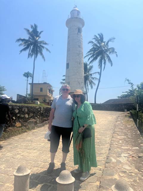 A couple posing in front of a lighthouse, with palm trees in the background.