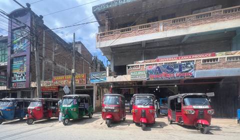 A row of colorful tuk-tuks parked in front of a building on a city street.