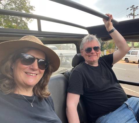 A couple smiling in an open-top vehicle, enjoying a sunny day.