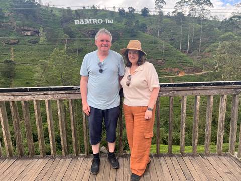 A couple standing on a wooden balcony overlooking a tea plantation.